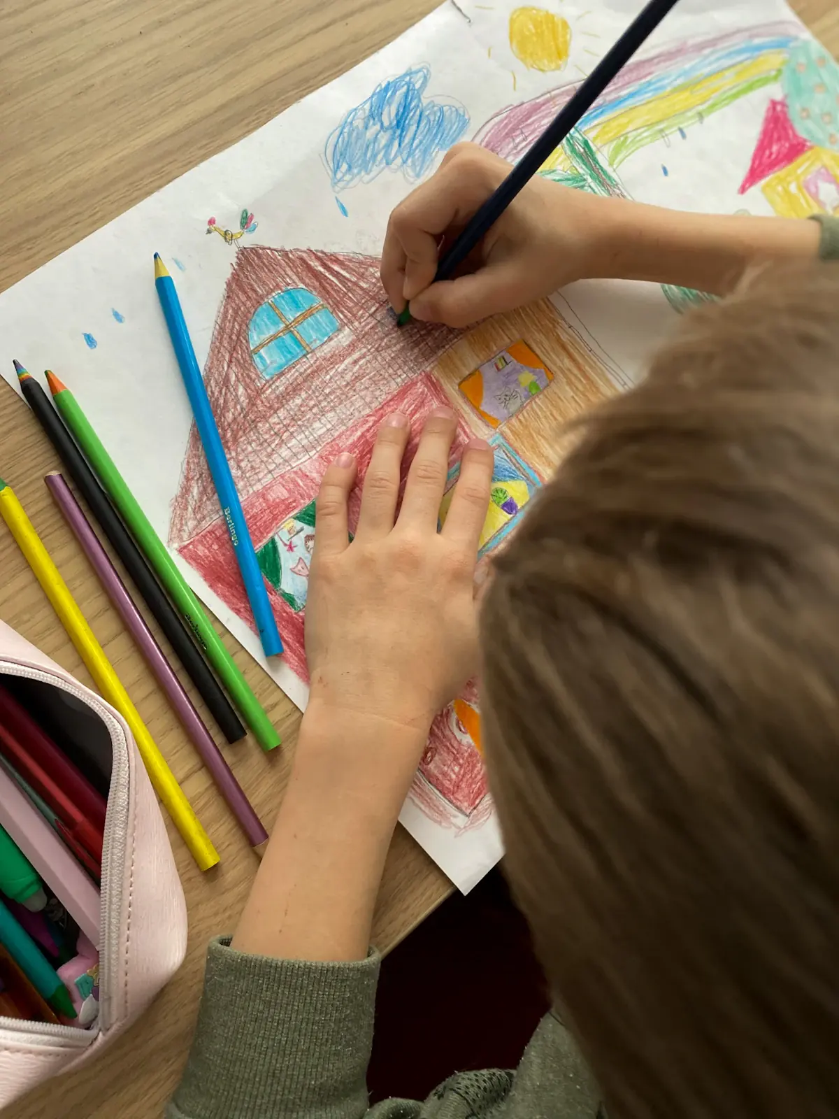 A child drawing a house in coloured pencil.